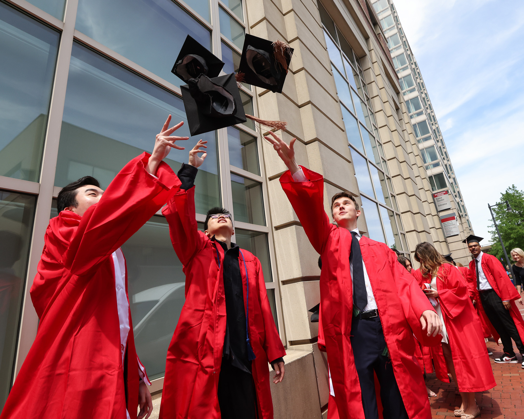 three grads in gowns throw caps into the air