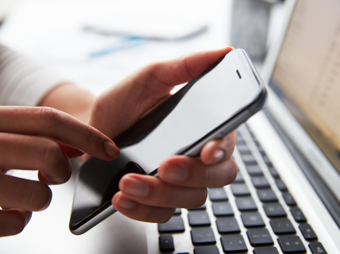 a person holds a phone while in front of their laptop
