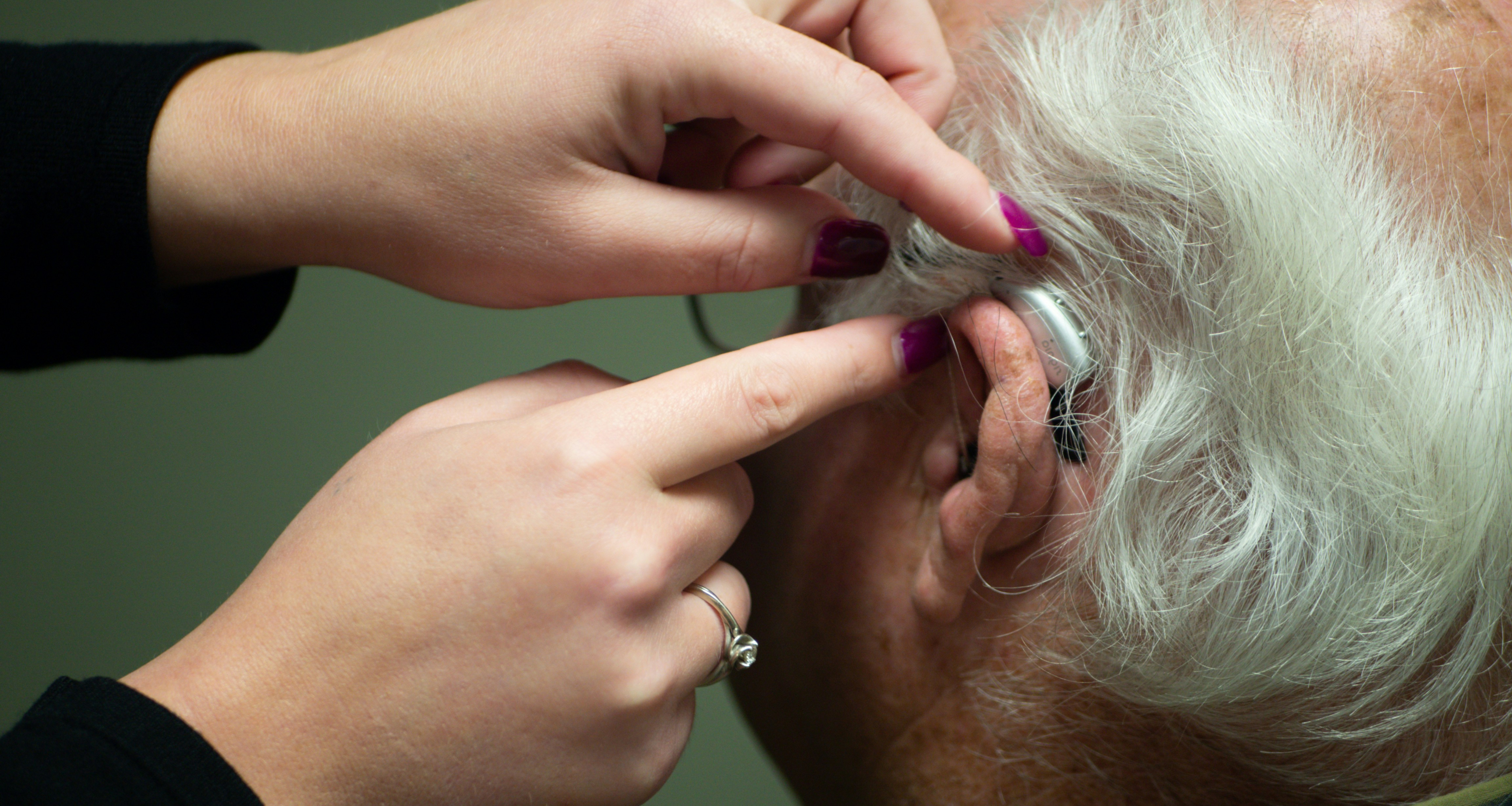 Doctor helps elderly man fit a hearing aid