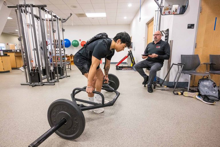 BU Physical Therapy Center staffer Andy Nhiv—under the watchful eye of BU researcher Trace Sears—demonstrates using an exosuit to assist with lifting weights