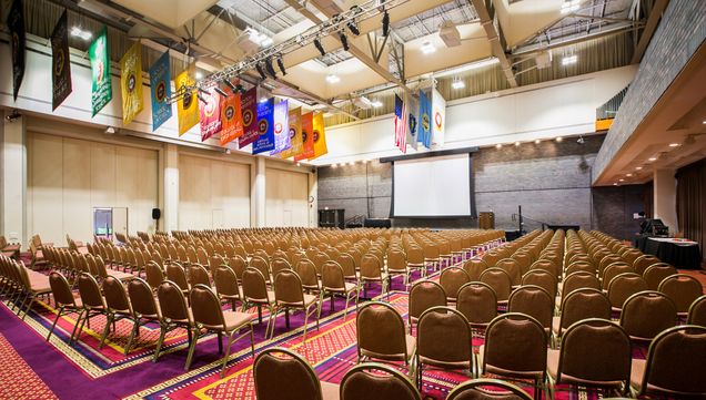 GSU Ballroom setup with rows of empty chairs with a white projection screen and school/college colorful banners overhead.