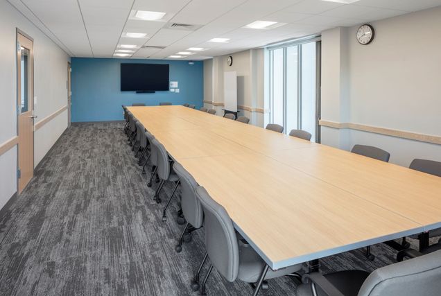 Long empty conference table & chairs within GSU 310 with TV mounted on a blue wall.
