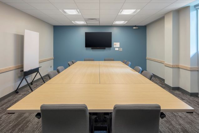 Empty view of room with long table, chairs around it, with a TV mounted on a blue wall.