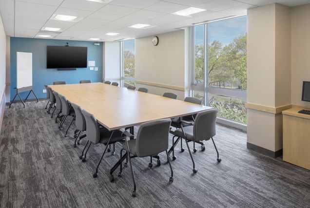 Empty room view with picturesque view out the windows, long conference table with chairs, TV mounted on blue wall, and moveable marker board in the corner.