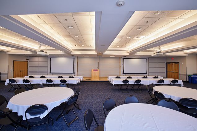 Room setup with round & rectangular tables with a BU podium and 2 screens for projection.