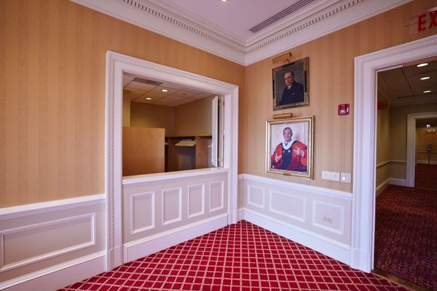 View of the Coat Room counter with white paneling and gold striped wallpaper, with two portraits of former BU presidents.