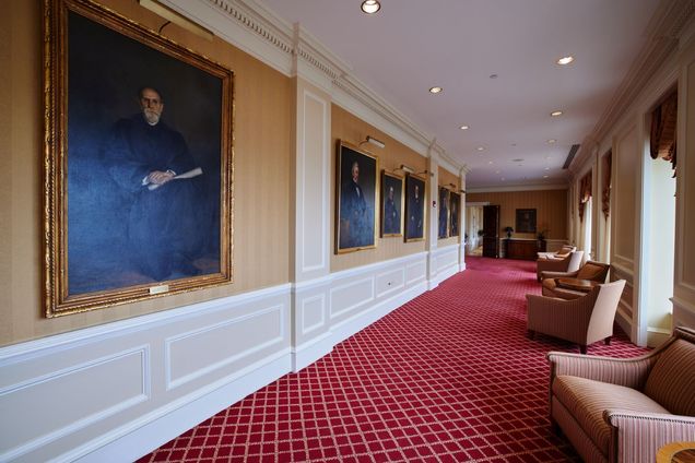 View of Portrait Gallery with red carpet, gold & white walls, with a series of painted portraits of BU presidents.