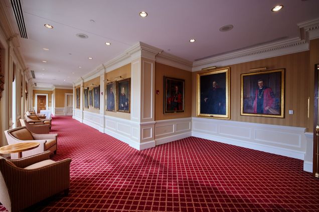 View of Portrait Gallery with red carpet, gold & white walls, with a series of painted portraits of BU presidents.