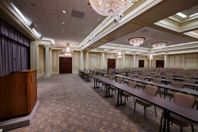 Empty Ballroom setup with grey chairs in rows, some with classroom tables, a podium with BU logo in the front next to a grey curtain.