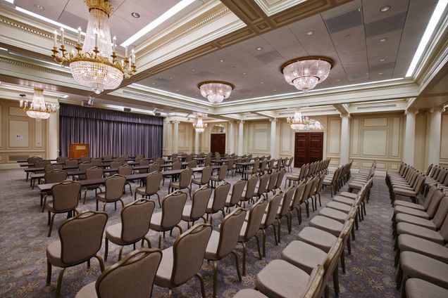 Empty Ballroom setup with grey chairs in rows, some with classroom tables, a podium with BU logo in the front next to a grey curtain.