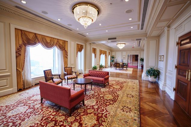 Long view of the Trustee Lounge, with ornate curtains, carpet, tables, chairs, and lounge furniture.