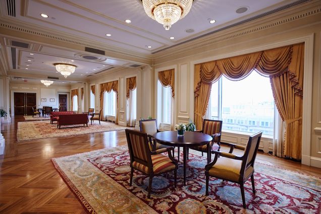 Long view of the Trustee Lounge, with ornate curtains, carpet, tables, chairs, and lounge furniture.