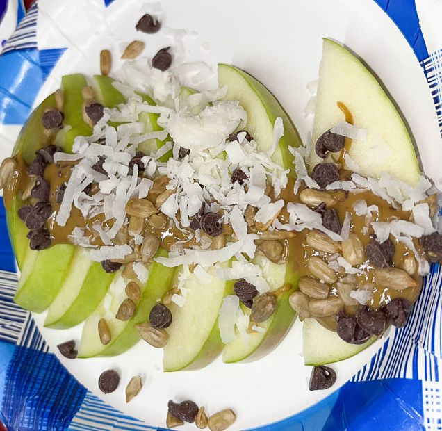Apple nachos cut and plated, topped with coconut flakes, chocolate chips, sunflower kernels, and sunflower butter.