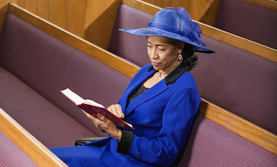 Senior African American woman sitting in pews reading Bible