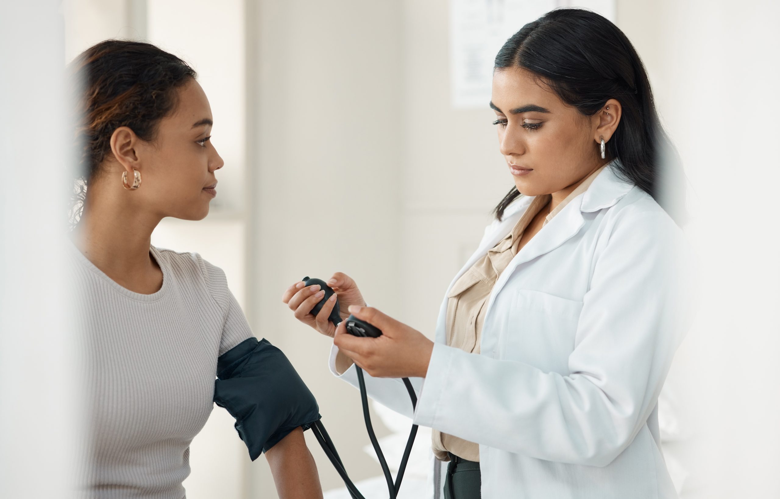 Shot of doctor standing and checking her patient's blood pressure during a consultation in the clinic