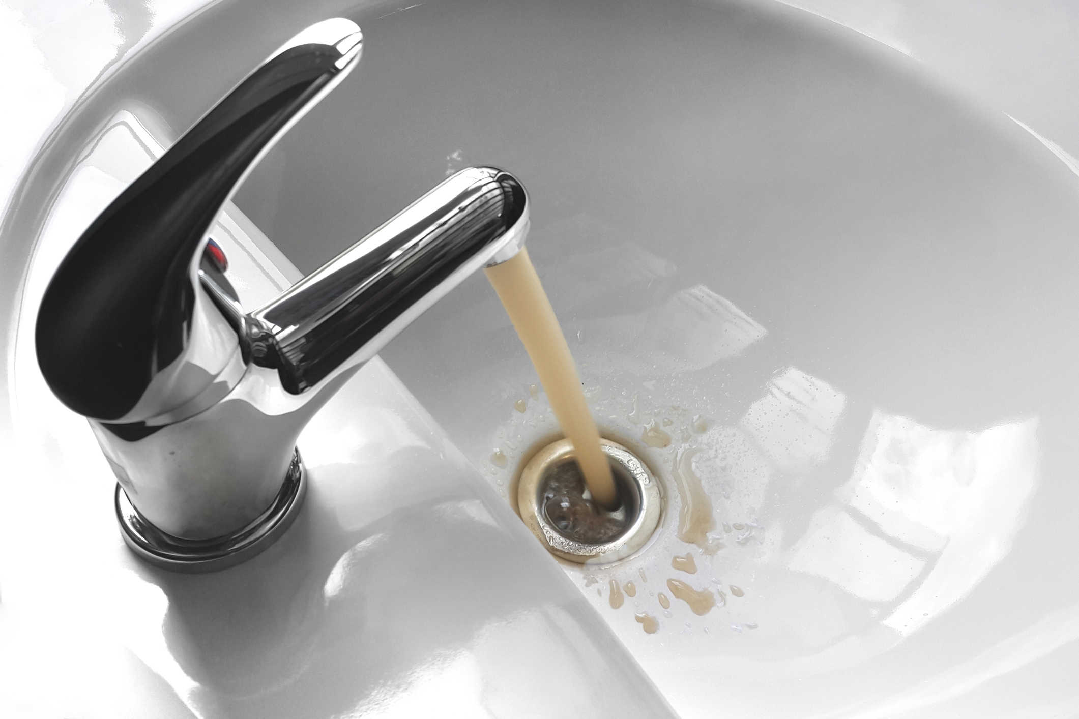 Water tap faucet with flowing contaminated muddy and dirty water in a white bathroom sink.