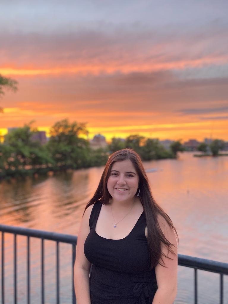 Headshot of Barbara Espinosa Barrera standing against a railing overlooking a river at sunset