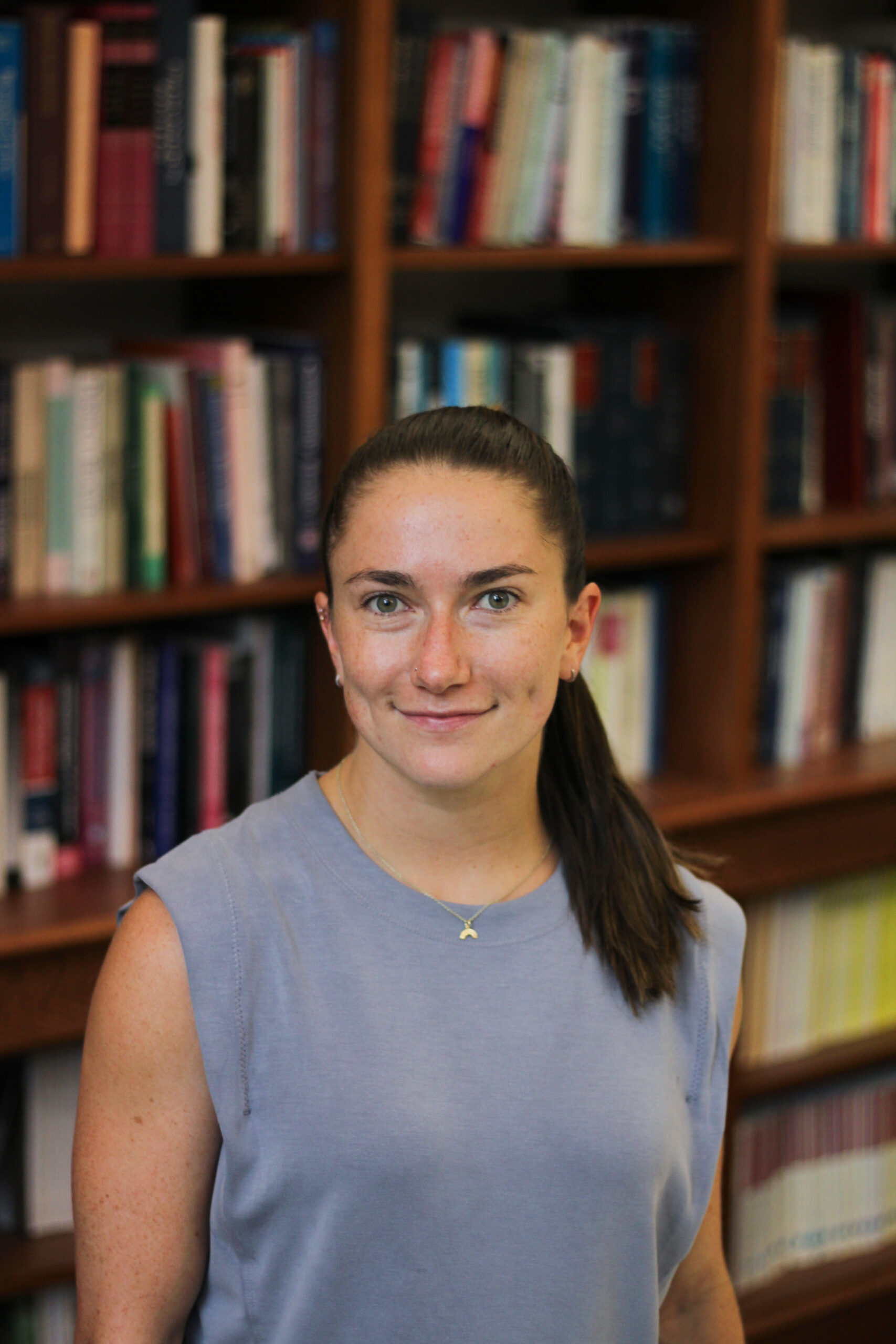 Malu Foley stands in front of a large bookcase and smiles at the camera