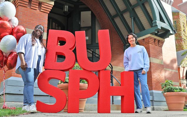 Students stand beside large red BUSPH letters