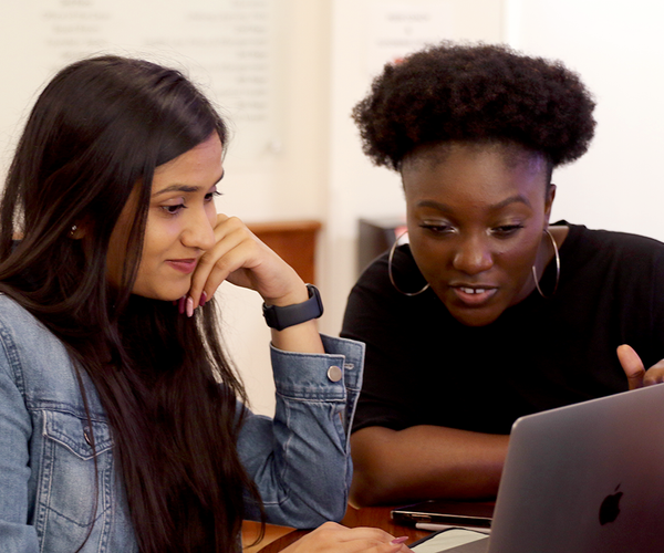 Two students discuss work around a laptop