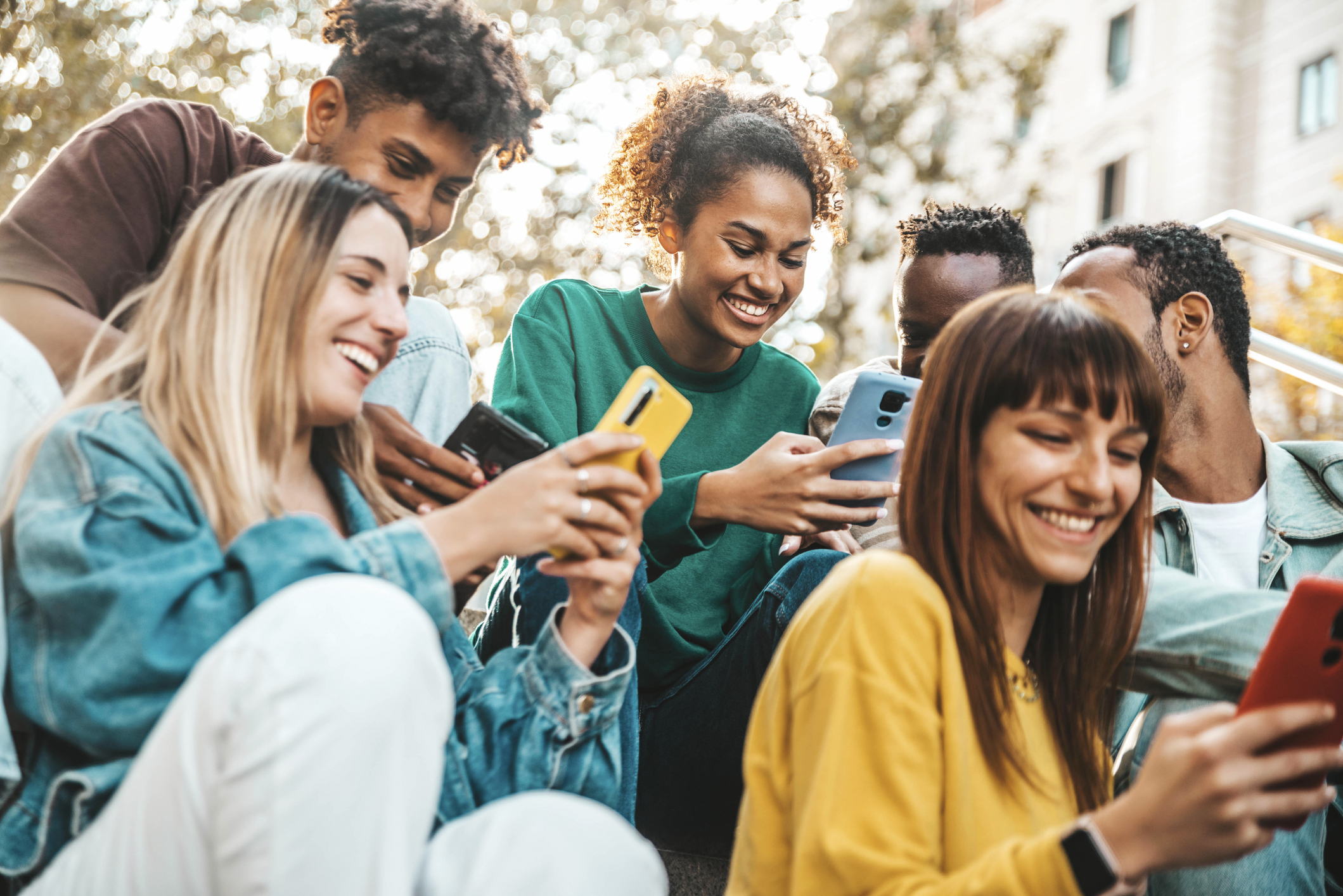 Happy university students watching cellphones sitting in college campus