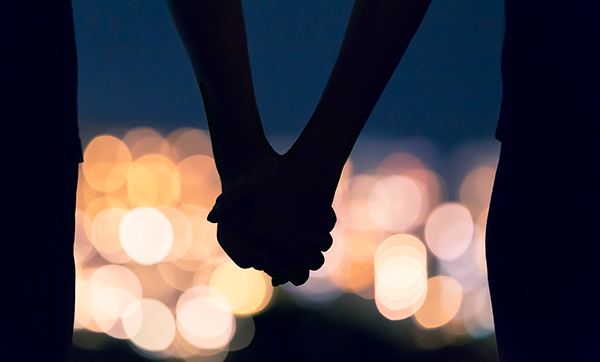 Couple holding hands against city night lights bokeh