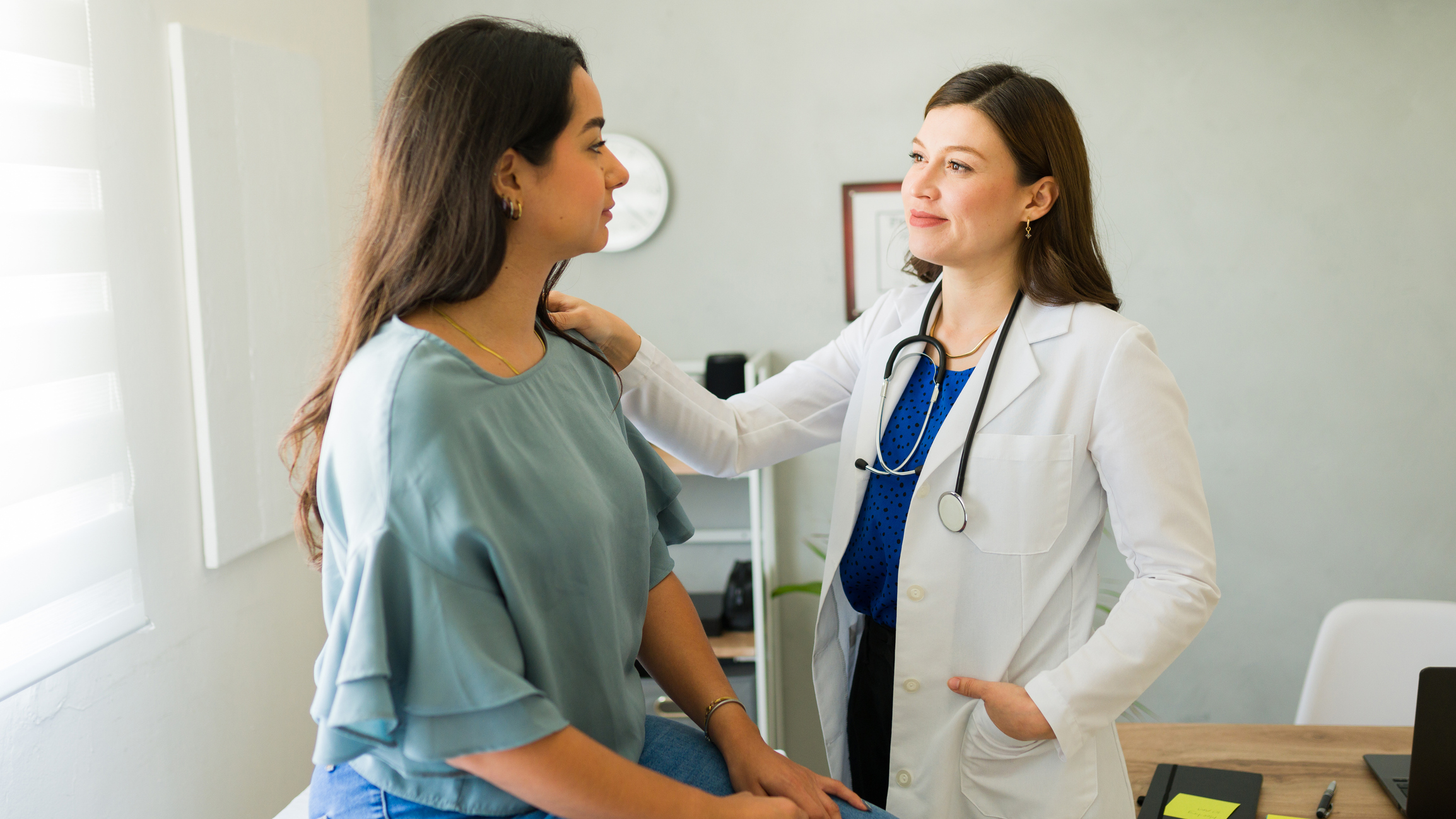 Woman doctor offers comfort to her patient by placing a hand on her shoulder during a diagnosis discussion in the doctor's office