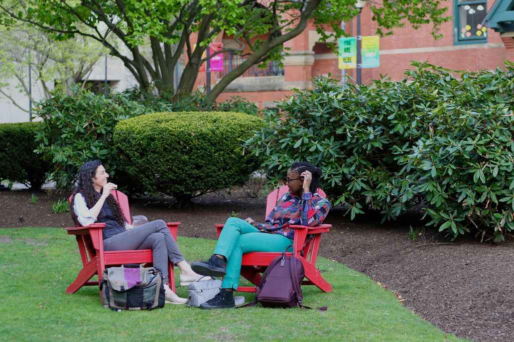 A pair of staff members having a bite to eat and a conversation in a pair of Adirondack chairs in front of the 托尔伯特建筑