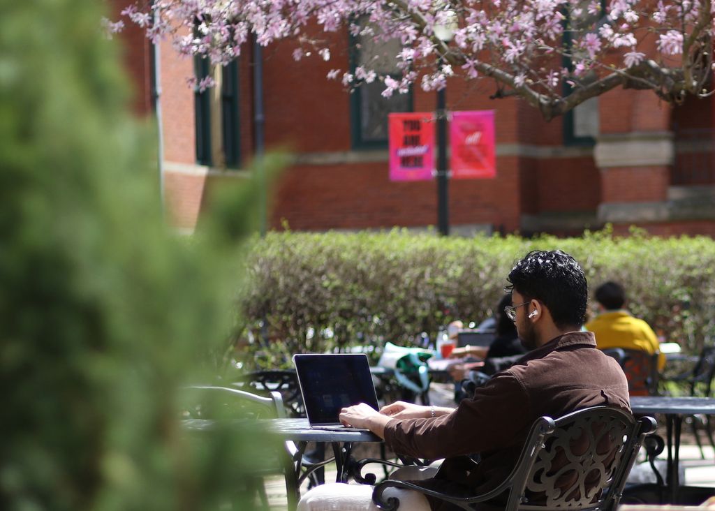 A student types on a laptop while sitting on the patio during a sunny day on the BU Medical Campus