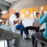 Latino male teen student receives praise from classmates. Multiracial group of high school 学生 sitting in a circle clapping together celebrating. Togetherness.