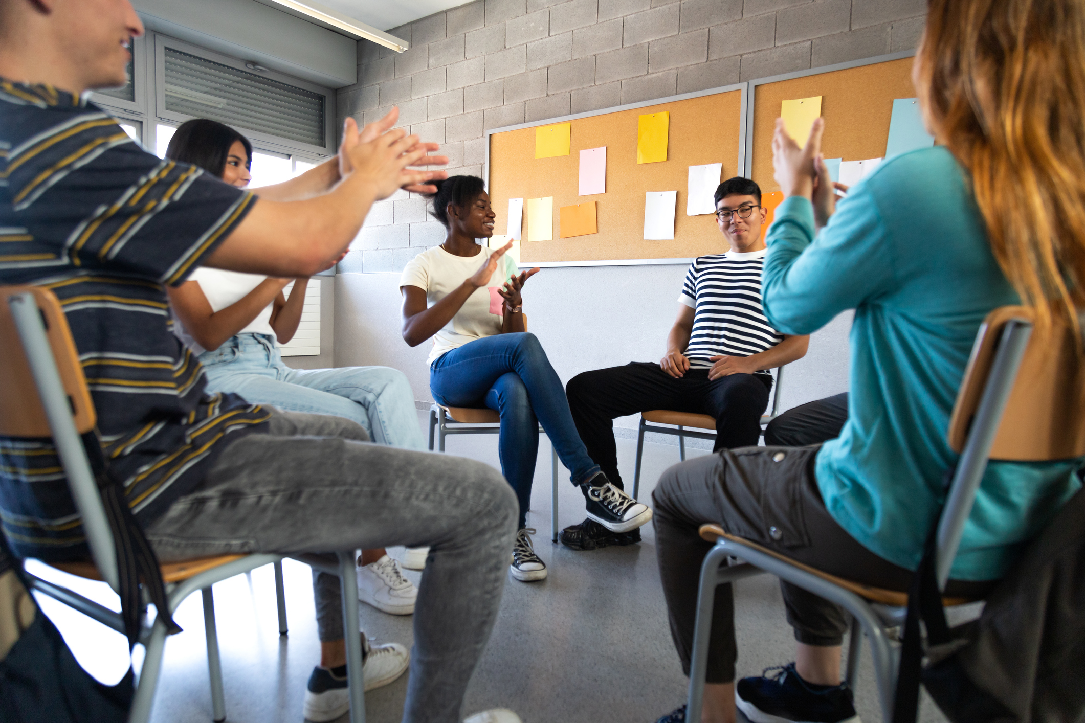 Latino male teen student receives praise from classmates. Multiracial group of high school students sitting in a circle clapping together celebrating. Togetherness.