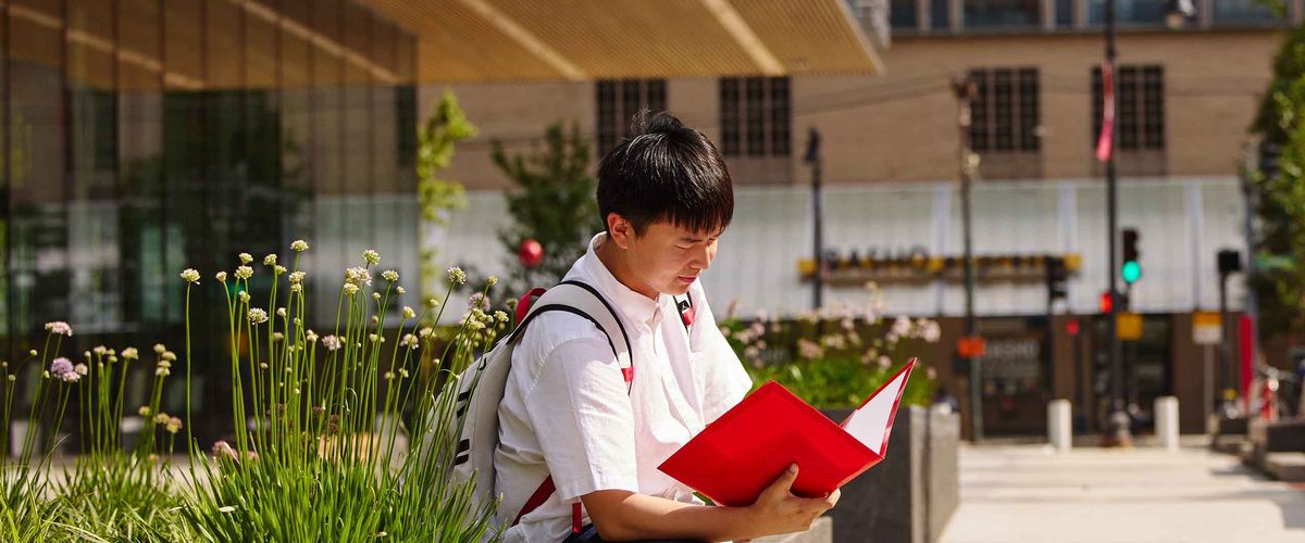 A student sitting in front of the BU Faculty of Computing & Data Sciences (CDS) building.