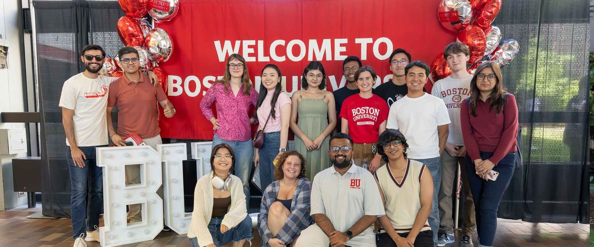 Students stand behind a Welcome to Boston University banner.