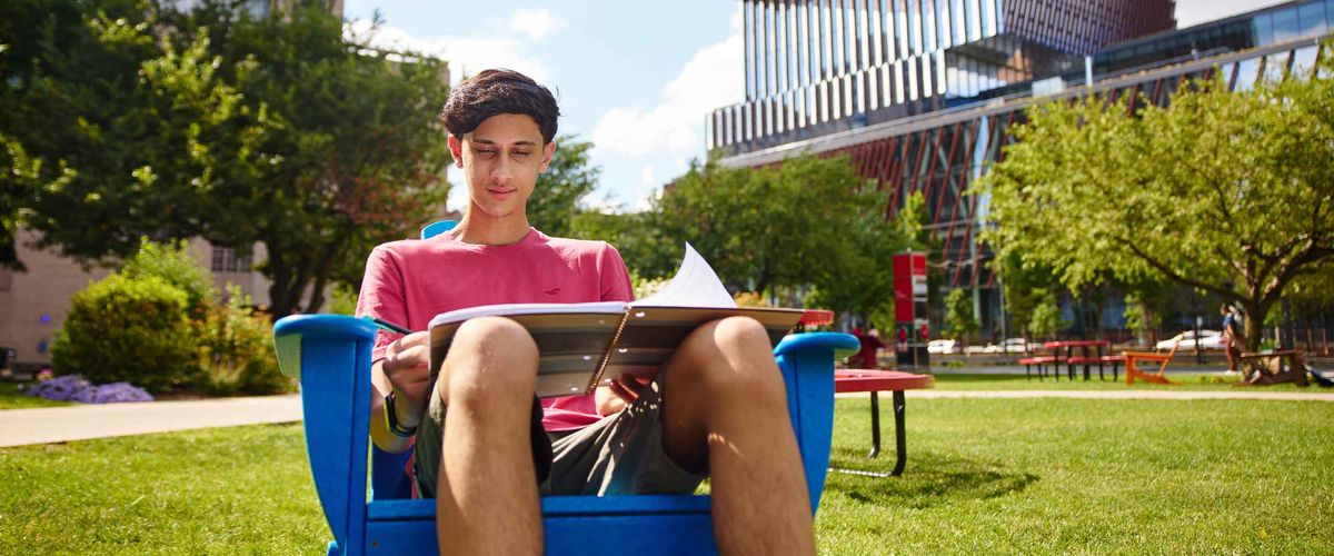 A BU Summer Term student doing homework on a lawn chair outside the Computing & Data Sciences building