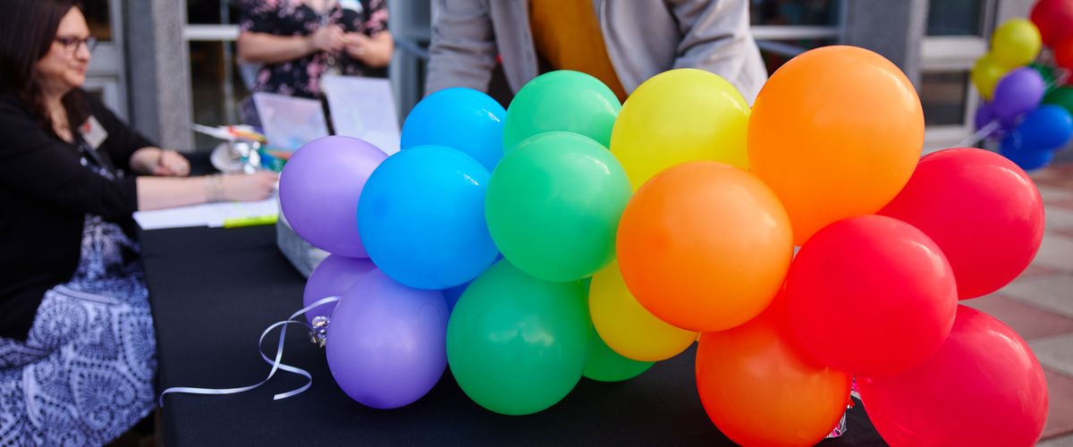A mini rainbow balloon arch on a check in table at an event with people checking in in the background.