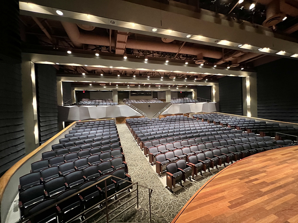 Interior view from stage of house seats in dark blue and carpeted aisles of gray.