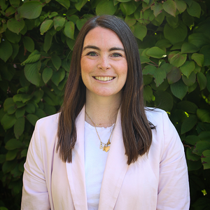 Headshot of Elizabeth Vassallo in a light pink blazer infront of a green bush