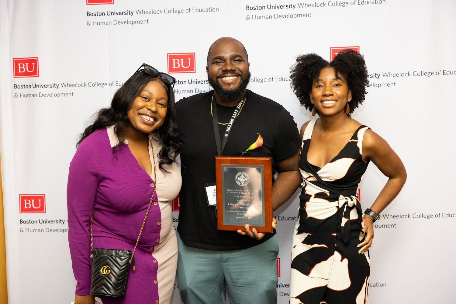 Cinique Weekes-Bynoe ('16) with guests holding there alumni award infront of the BU Wheelock backdrop