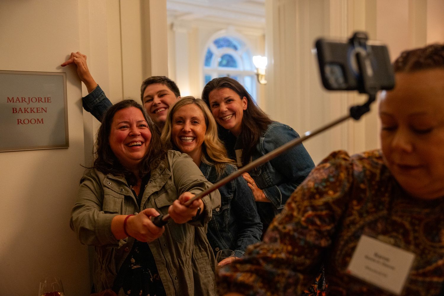A group of alumni taking a selfie with the sign for the Marjorie Bakken Room.