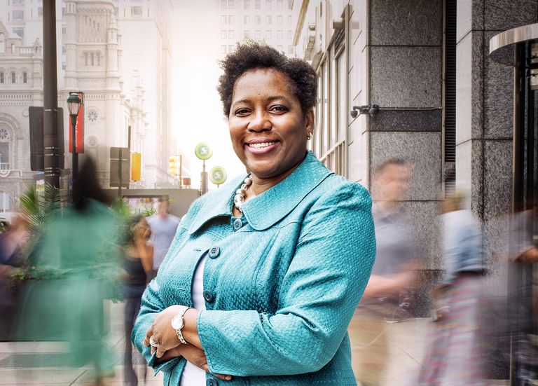 Leah Hollis in light blue on city street standing with her arms crossed smiling