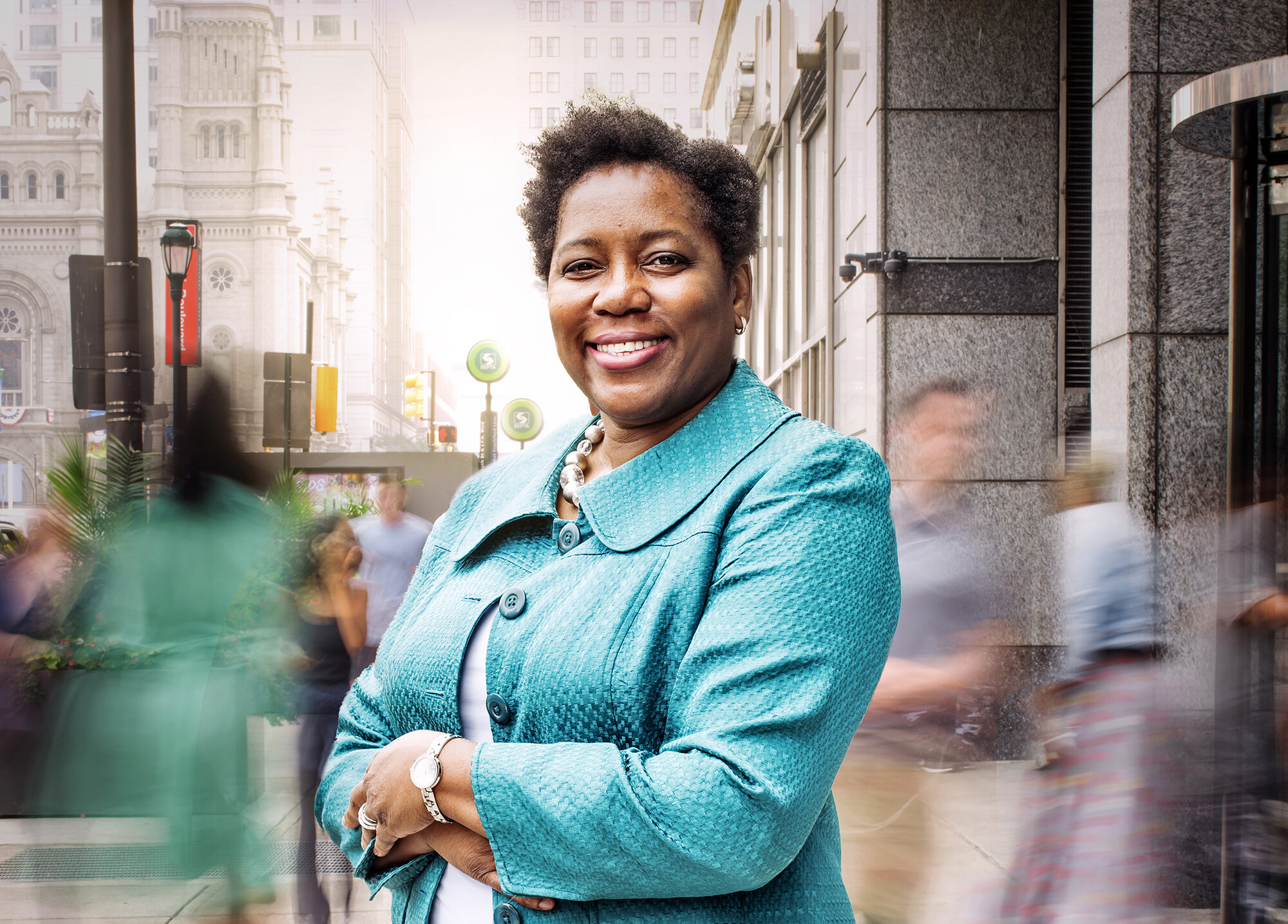 Leah Hollis in light blue on city street standing with her arms crossed smiling