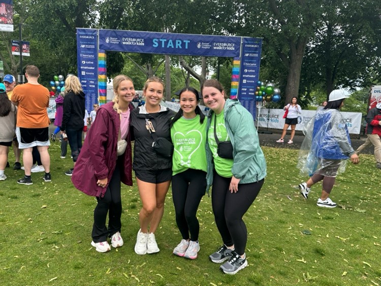 Four young women dressed for exercise pose in front of a sign that says Walk for Kids