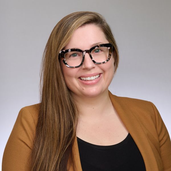 Photo of Lauren Funk, who has long hair and is wearing glasses, a black top, and brown jacket