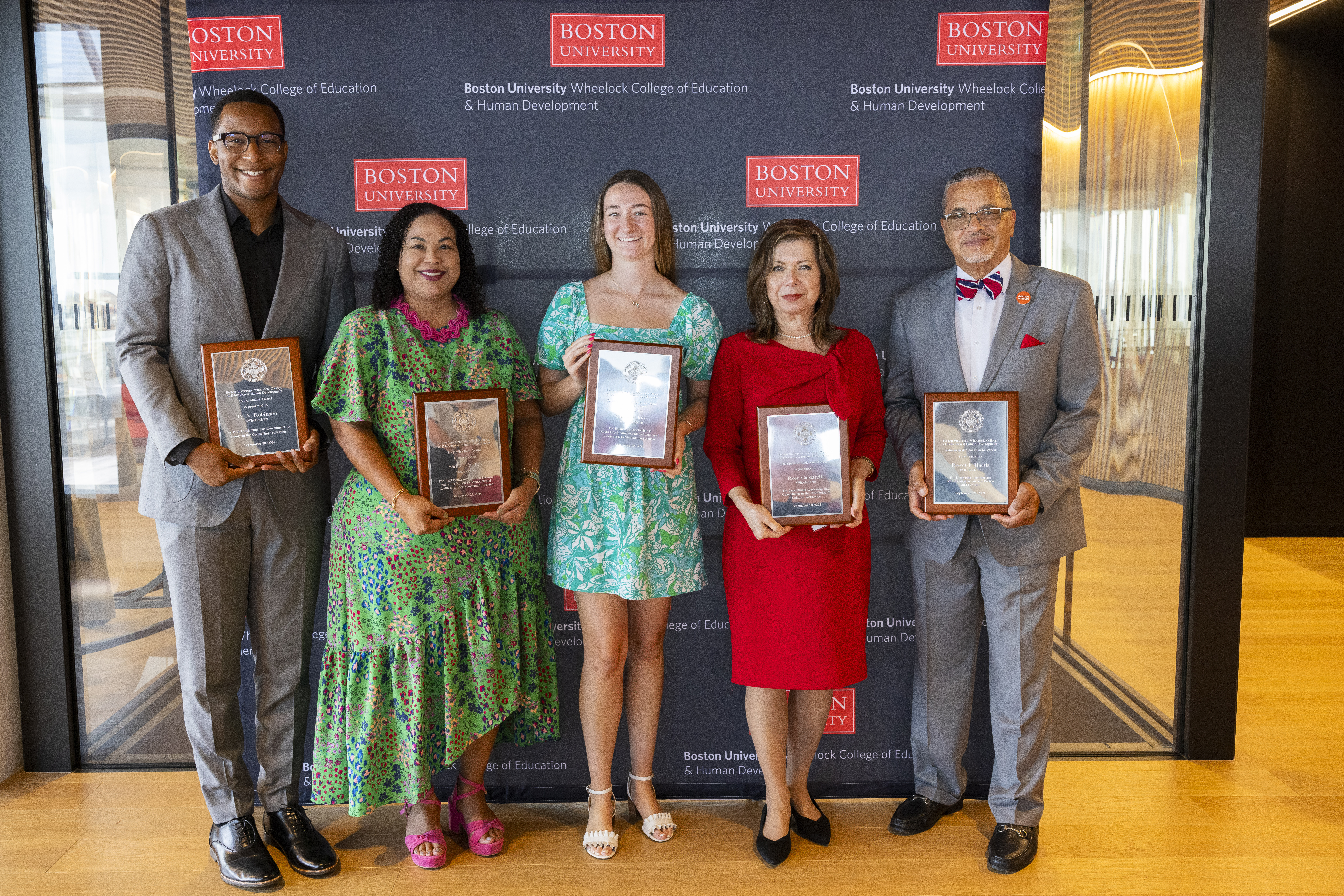 The five alumni award winners standing with their awards infront of a black step and repeat reading Boston University Wheelock College