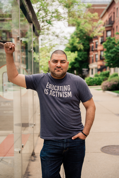 Raul Fernandez looking at the camera with a grey t-shirt reading "Educating is Activism"