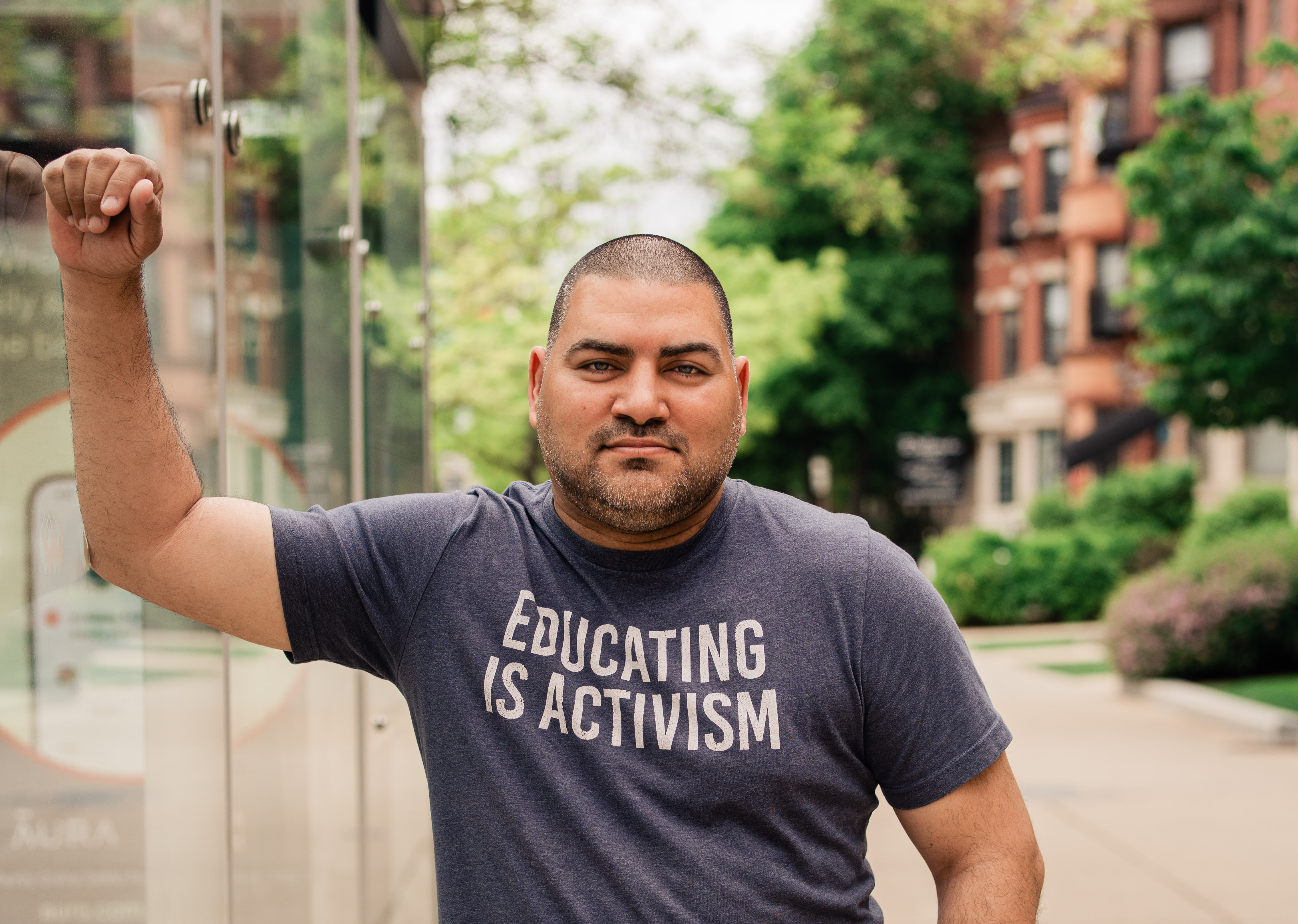 Raul Fernandez looking at the camera with a grey t-shirt reading "Educating is Activism"