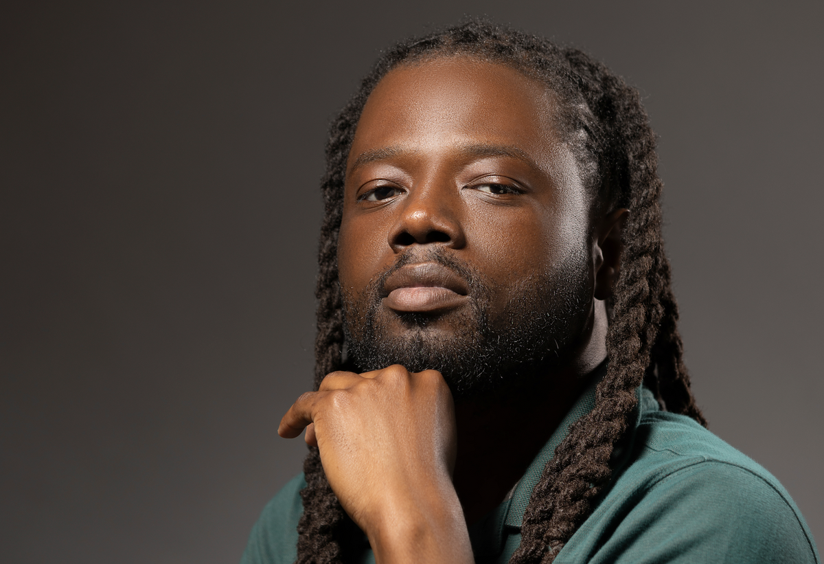 Franklin Jones Jr in green polo shirt stands posed with his chin resting on his hand