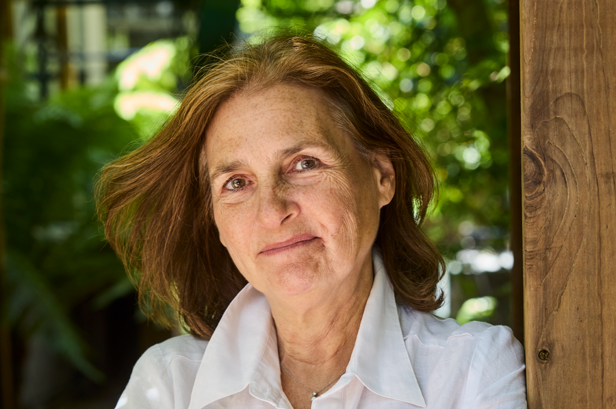 Deb Buehler stands smiling in a white button down leaning on a wooden beam