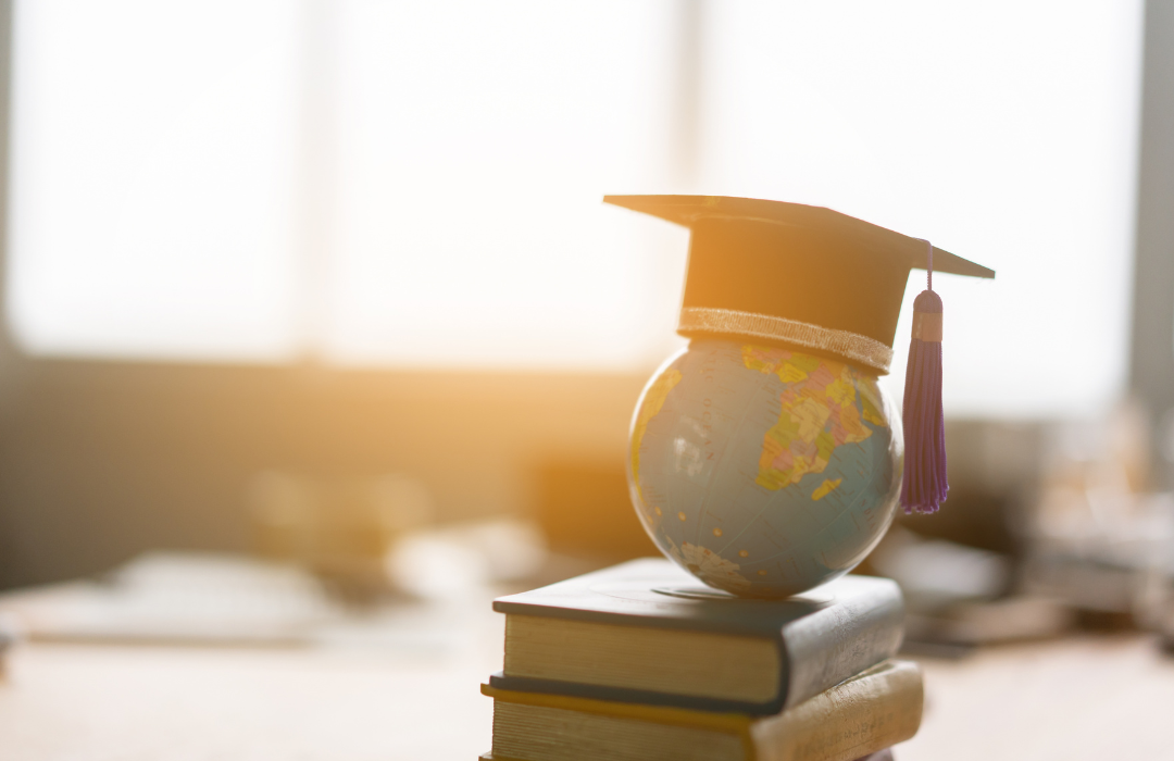 Small globe stacked on books wearing graduation cap
