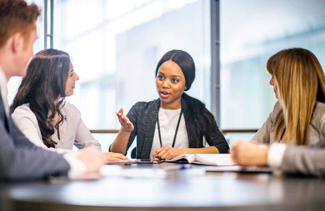 Young women leading meeting around a table with other professionals